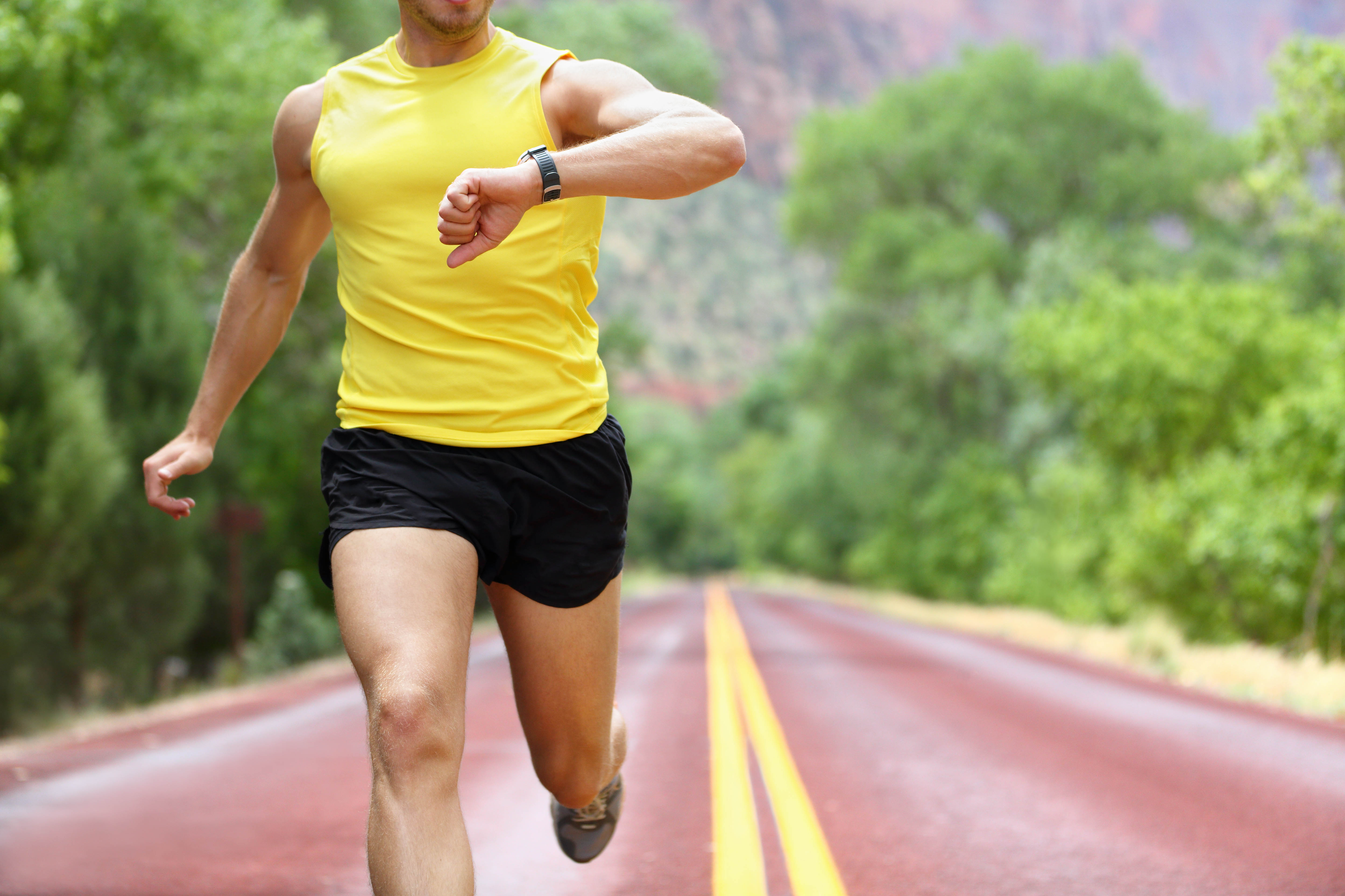 Torso of a fit man in a yellow shirt running on a track, checking his smart watch